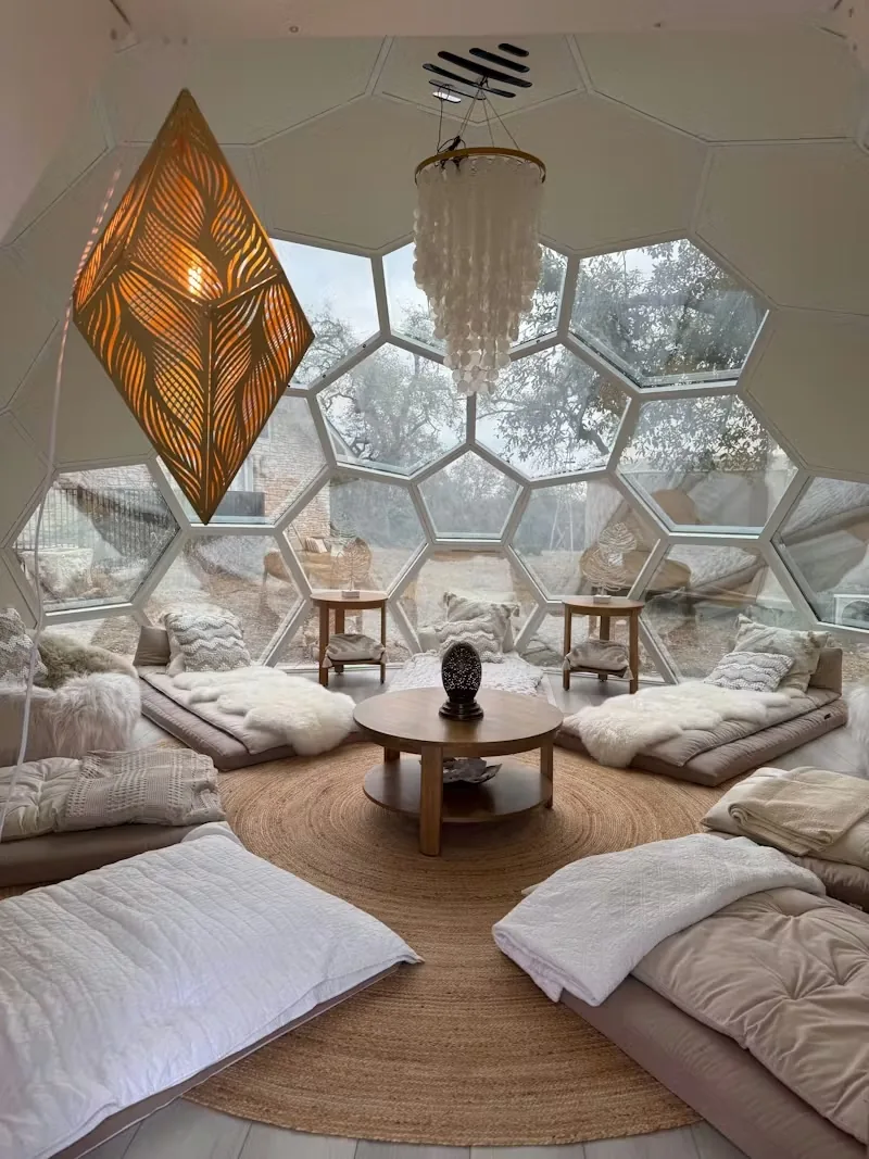 Two chairs and a low table in a small glass dome, the oaks beyond