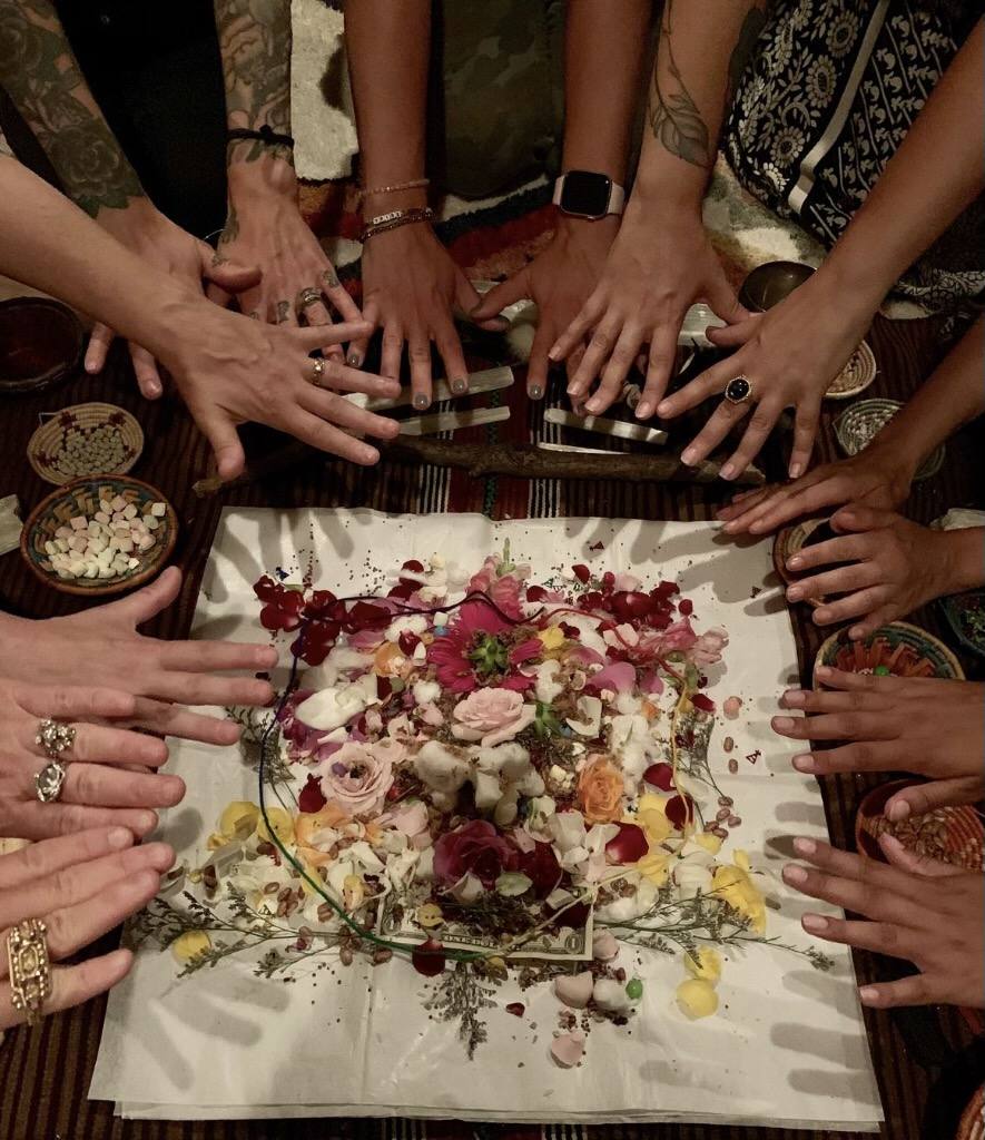 Hands joined in circle around an offering of flowers