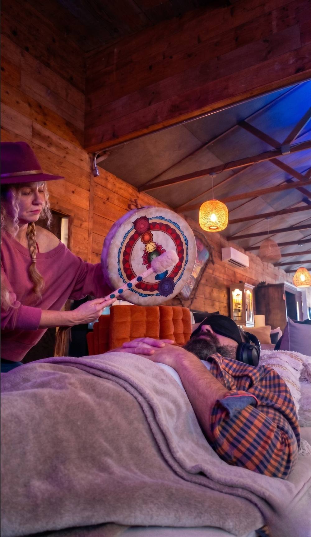 A facilitator sounding a painted drum over a resting participant